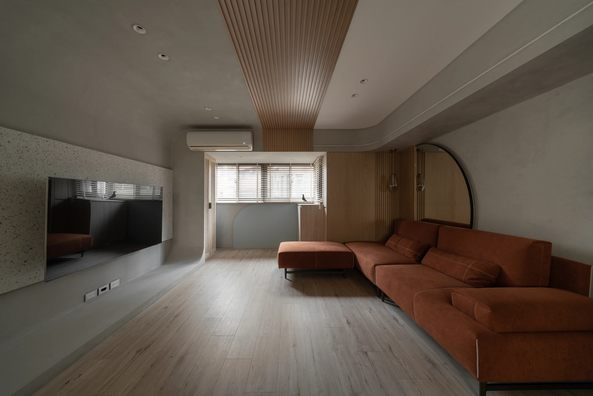 新竹舊屋翻新客廳,磚橘絨布沙發與磨石子拱形電視牆、圓鏡與木格柵天花 — 覺壹設計